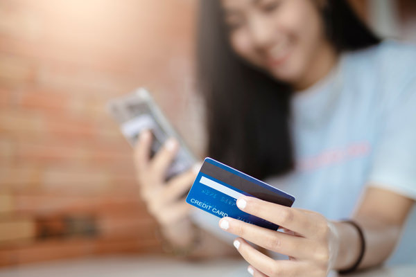 An out of focus woman holds a phone and a credit card, which is in focus