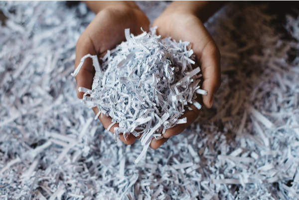 Two hands hold a small pile of shredded paper, more lies underneath